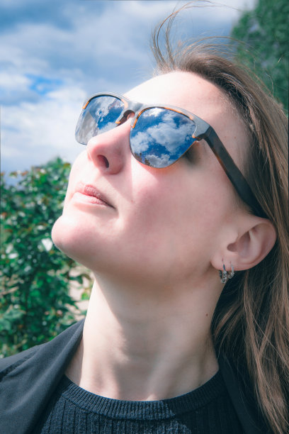 戴着太阳镜的女人看着天空中云朵的倒影图片下载