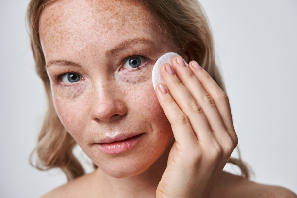 满脸雀斑的漂亮女人用化妆棉清洁她的脸图片下载