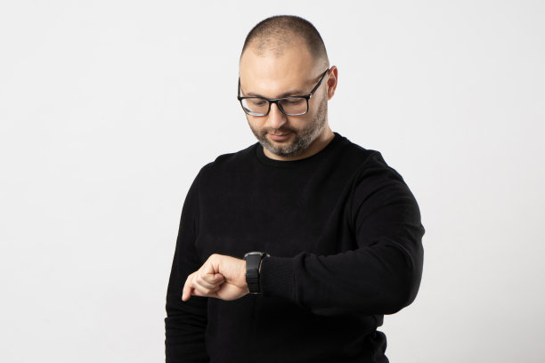 一个戴着黑框眼镜、穿着黑夹克的人看着他的手表图片下载