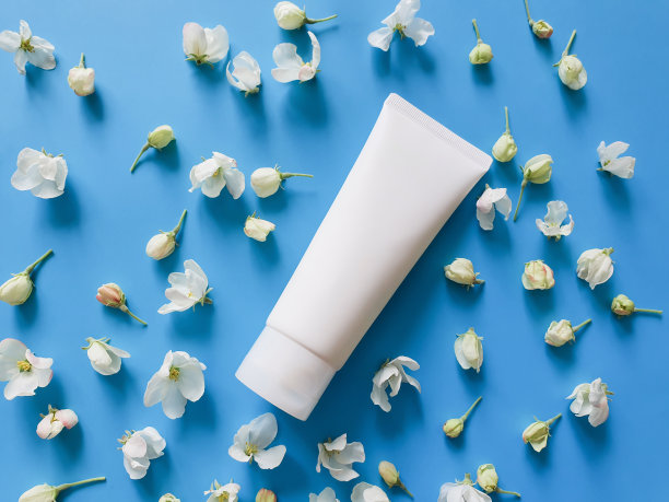 白色塑料管品牌和小白花在饱和的蓝色背景。SPA美容产品。花平躺和模拟。俯视图图片下载