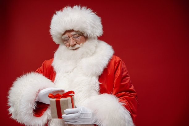 善良的圣诞老人抚摸着红色背景上的小礼品盒图片下载