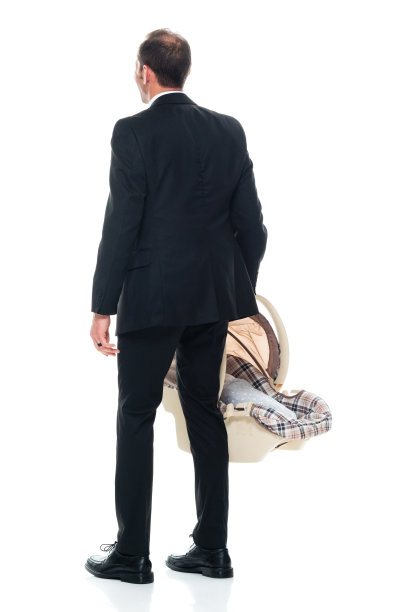 白人婴儿-人类年龄站在白色背景前，穿着商务服装，拿着汽车安全座椅图片下载