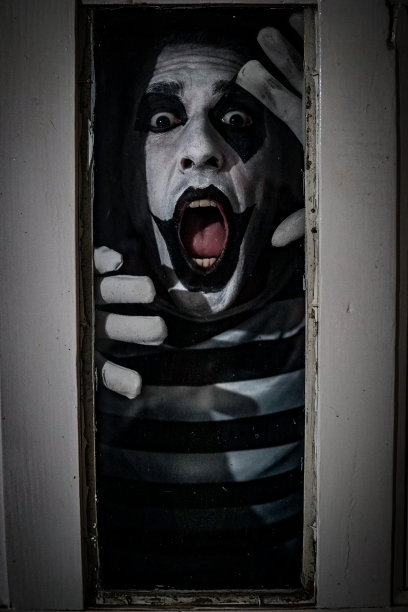 一个穿着哑剧服装的男人在一扇生锈的旧门的窗户后面恐怖地摆姿势图片下载
