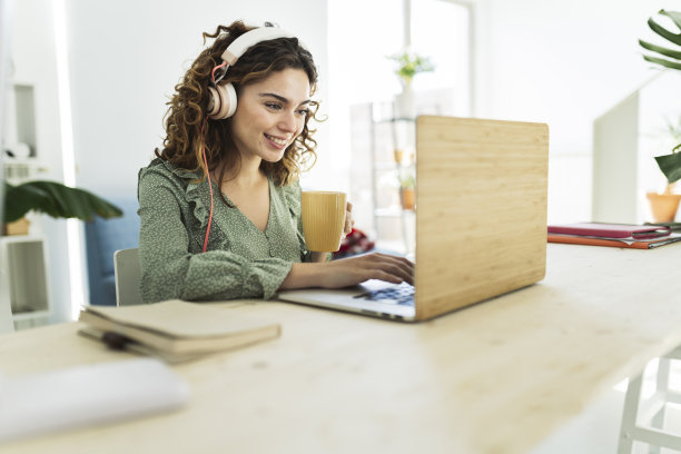 漂亮女人用电脑，带着耳机，在家喝着饮料图片下载