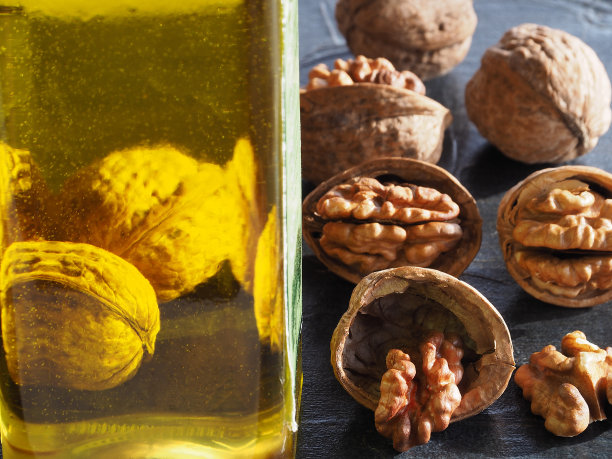 核桃仁和透明瓶核桃果油在黑暗的背景，特写镜头。一个明亮的模板，健康的天然产品从坚果为适当的营养。图片下载