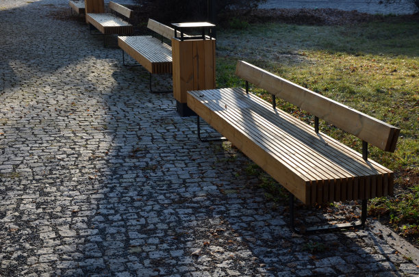 木制长长凳，座位区由一排排垂直木板和靠背组成。在工作台的边缘可能有凹槽，用于插入自行车轮胎。多年生植物的公园图片下载