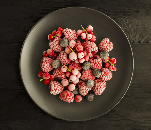 冷冻浆果在黑色盘子中央的黑色木质背景。前视图。图片下载