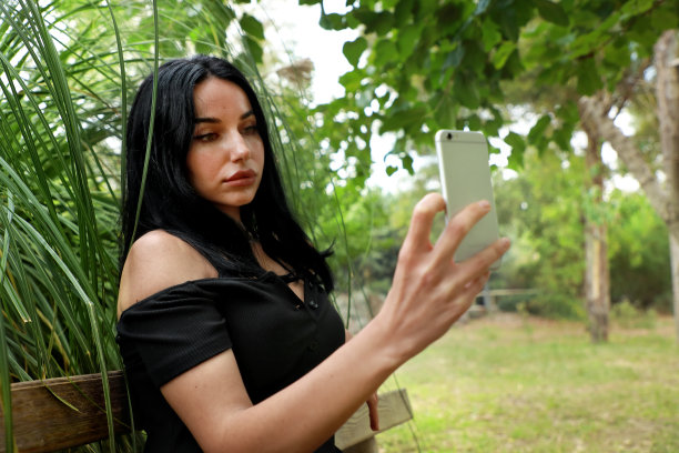 户外肖像年轻的成年白人妇女坐在公园长椅和使用电话图片下载