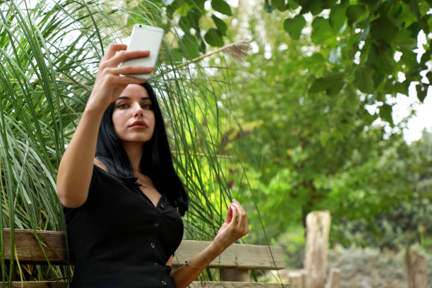 户外肖像年轻的成年白人妇女坐在公园长椅和使用电话图片下载