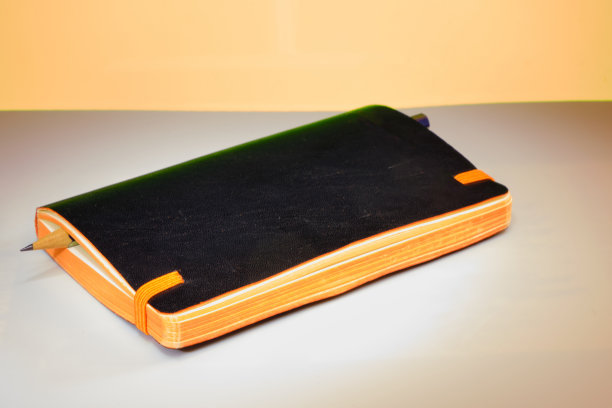 黑色皮革织物精装笔记本或moleskine弹性带背和橙色叶子孤立的背景。图片下载