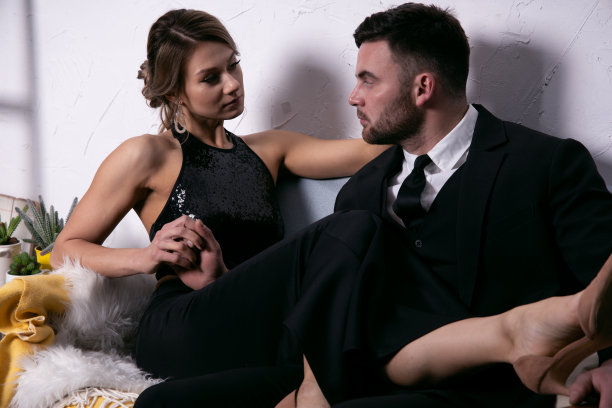 性感的女孩把她的脚放在她优雅的男人的大腿坐在沙发上。一对情侣相爱的复古肖像图片下载