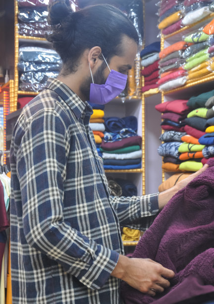 冠状病毒大流行期间，一个戴着口罩的帅气年轻人在服装店看买的衣服图片下载
