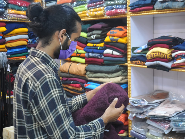 冠状病毒大流行期间，一个戴着口罩的帅气年轻人在服装店看买的衣服图片下载