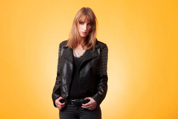 一个迷人的金发女人穿着饰钉皮夹克在黄色背景的肖像图片下载