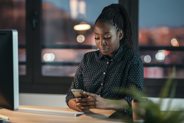 美丽的商业女人发送信息与移动电话在办公室工作。图片下载