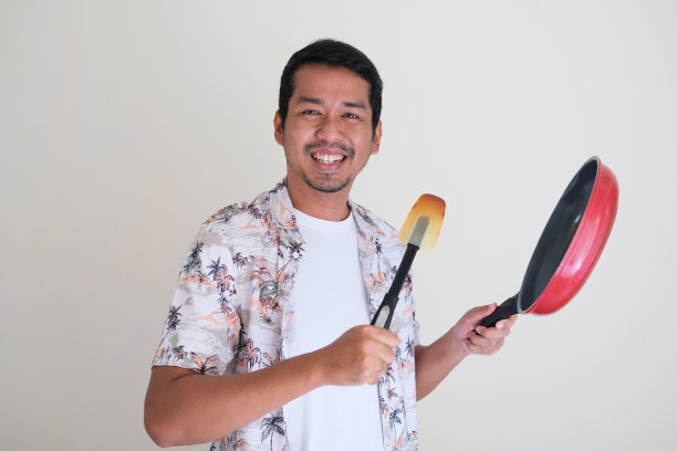 在厨房做饭时拿着煎锅和刮刀的亚洲人图片下载