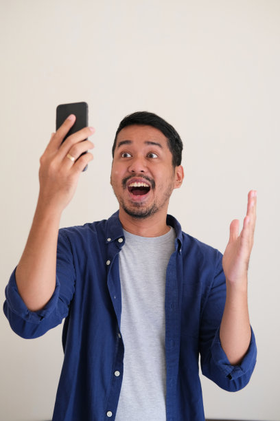 亚洲成年男子在看他的手机时表现出惊讶的表情图片下载