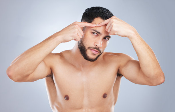 一名年轻英俊的男子摸着自己的脸，在工作室灰色的背景下看起来很不高兴图片下载