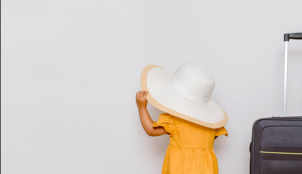 一个戴着白色超大帽子的小女孩的后视图，旁边是一个大箱子。图片下载