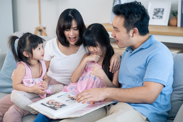 亚洲家庭看着旧相册上的照片回忆过去。年轻漂亮的夫妇和年幼的女儿坐在一起，翻动着相册，享受着回忆彼此关系的时光。图片下载
