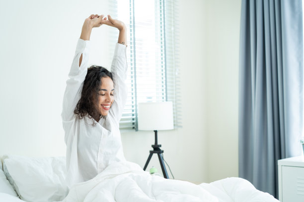 美丽的拉丁裔女孩穿着睡衣在早上醒来的幸福。迷人的年轻女子微笑着，感到快乐和放松，然后伸展身体后，从床上的卧室在家里。图片下载