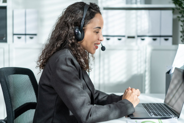 美丽的拉丁裔商务女性呼叫中心微笑，而工作在办公室。漂亮的年轻女员工穿着正装坐在工作场所的桌子上，用笔记本电脑交谈来支持客户。图片下载