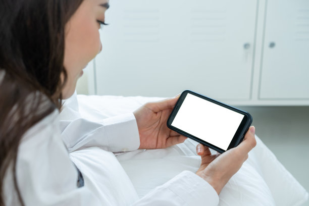 亚洲女性在家床上用白屏在线视频通话。美丽迷人的女孩穿着睡衣享受在早上醒来后在卧室用手机讲虚拟远程在线。图片下载