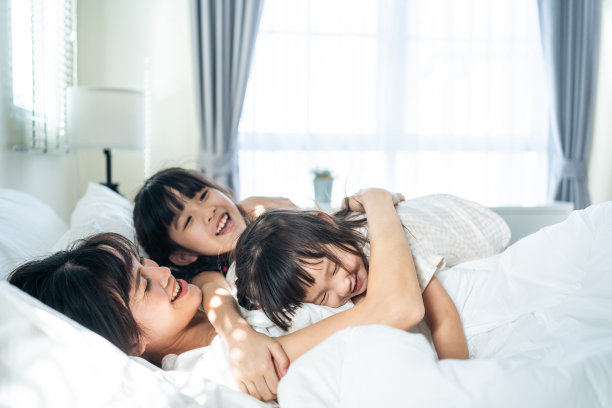 亚洲快乐的孩子早上跳到床上叫醒妈妈。年轻的小女孩和兄弟姐妹喜欢在卧室里和可爱的妈妈一起快乐地玩耍。活动关系的概念图片下载