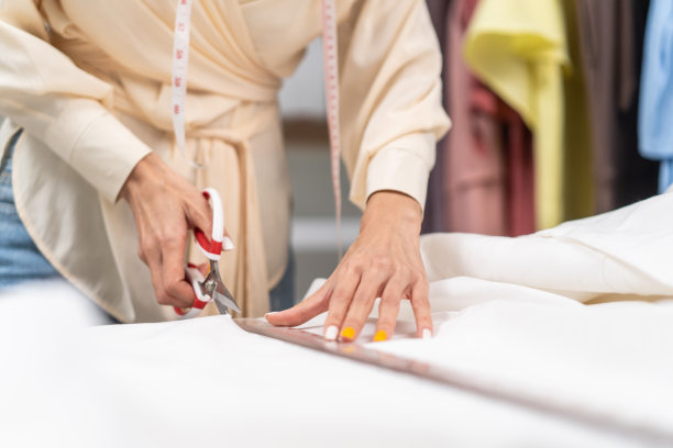 近距离的亚洲裁缝妇女工作在裁缝工作室的布料。迷人的年轻女孩时装设计师，裁缝用剪刀在车间的桌子上裁布。时尚的经营理念。图片下载