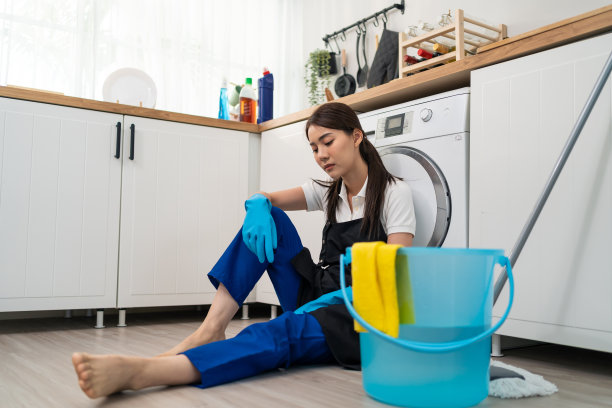 亚洲年轻的家庭主妇在做家务后感到筋疲力尽。有魅力的女管家清洁工坐在地板上，感到疲惫和压力，清洁厨房和过度工作的房子。图片下载