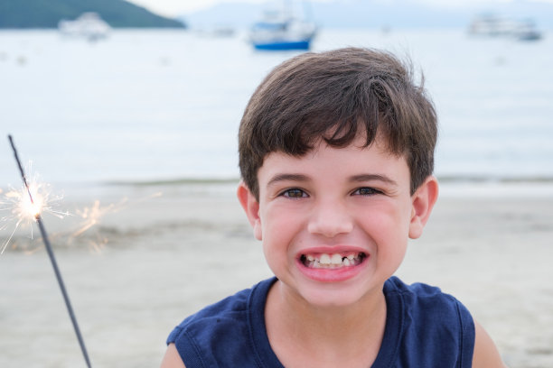 一个微笑的巴西孩子的特写，拿着蜡烛在沙滩上闪闪发光。图片下载