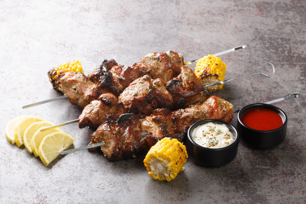 自制的烤肉串与烤玉米，柠檬和两种酱汁在混凝土背景上的特写镜头。水平图片下载