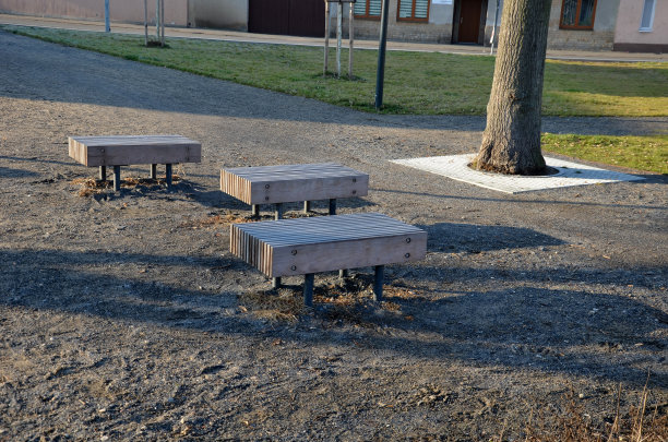 木制的小长凳，座位部分由一根杆连接的一排排垂直木板组成。公园在冬季与多年生atravinali。太阳照亮了这个空间。周围防护栅格图片下载