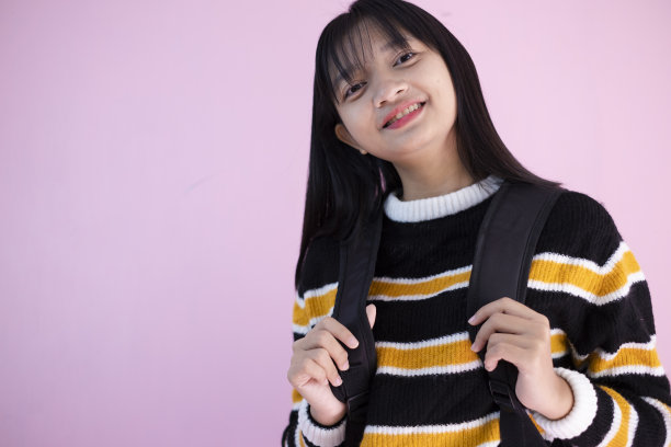 快乐的年轻女孩与粉红色背景的背包。图片下载