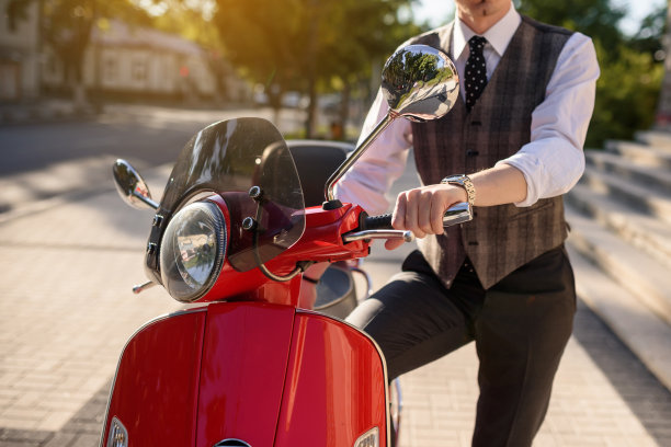 一个穿着经典背心的男人在一辆红色老式摩托车旁。图片下载