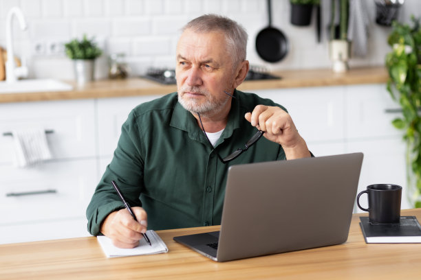 沉思严肃的老人，带着笔记本电脑坐在家里的桌子旁图片下载