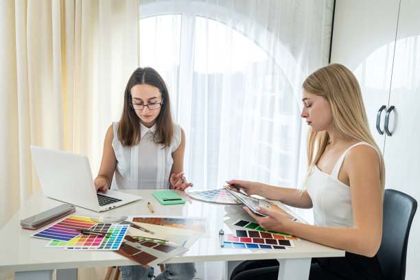 两个漂亮的女孩设计师坐在桌子旁，为房间的设计选择颜色图片下载