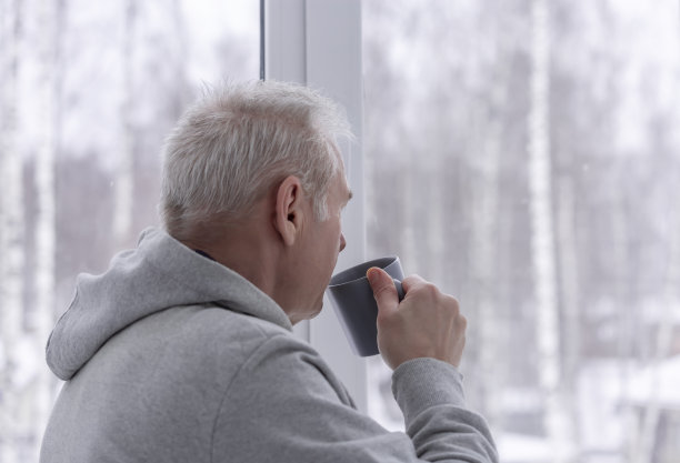 一个拿着杯子望着窗外的男人图片下载