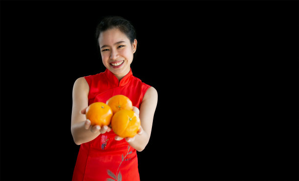 快乐的亚洲妇女穿着红色旗袍，用拷贝空间展示促销广告，面带微笑，拿着橙子庆祝中国新年。图片下载