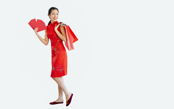 全身美丽开朗的亚洲妇女穿着红色旗袍，微笑着，举着旗袍，购物袋在白色的背景与拷贝空间，现在促销广告，庆祝中国新年。图片下载