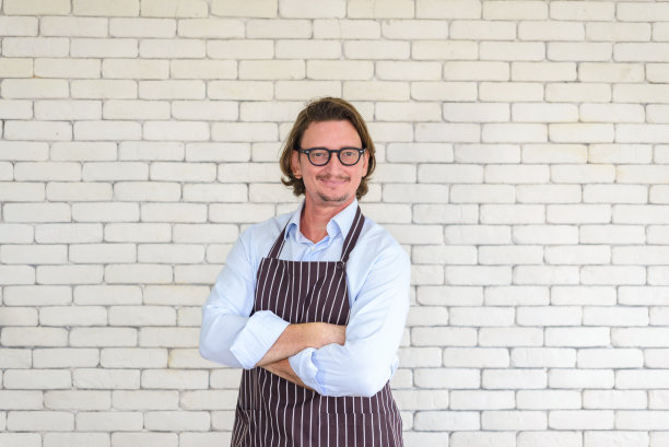 快乐的高级男子的肖像园艺戴眼镜和牛仔围裙站在白色砖的背景与自由空间或文本复制空间。看相机。图片下载