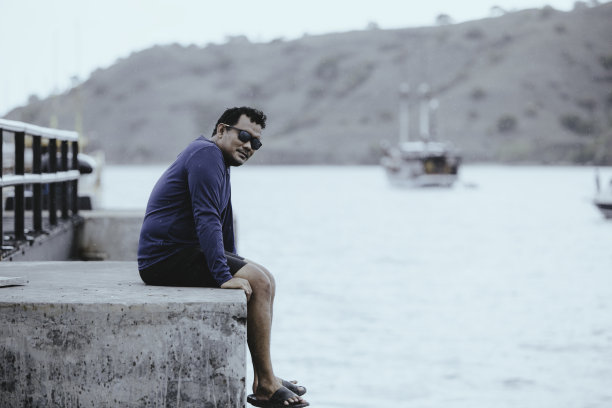 年轻的亚洲男子坐在桥上看着相机图片下载