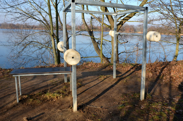 一个户外家庭健身房坐落在湖边。中国人有混凝土砝码，而且被拴在链子上。健身酒吧，卧推，自行车道，水坝，草地图片下载