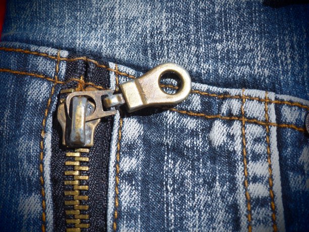 特写牛仔布与接缝和锁。破旧不堪的牛仔裤。金属青铜黄色锁带流道。垂直接缝。图片下载