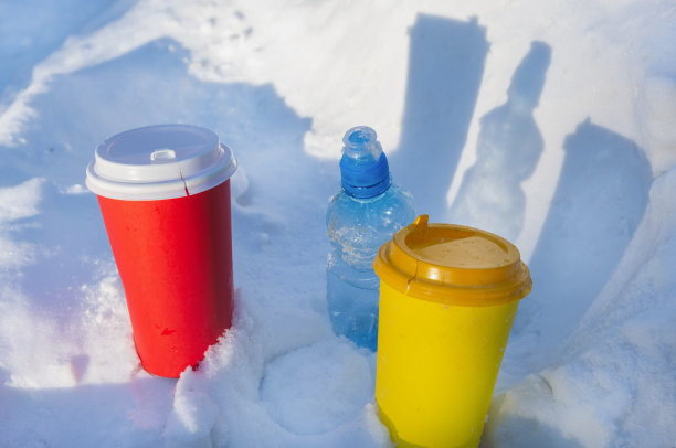 五颜六色的咖啡杯和一个塑料瓶插在雪地里。生活垃圾环境污染概念图片下载