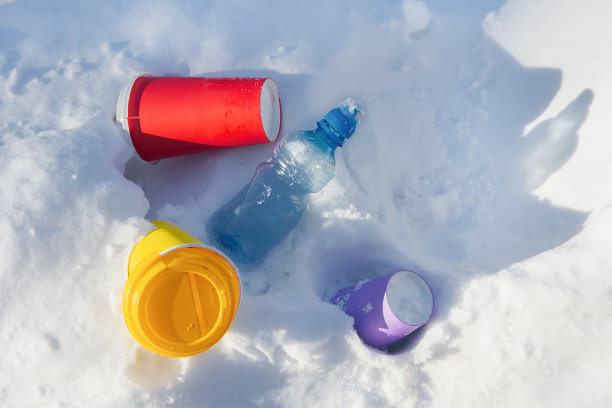 五颜六色的咖啡杯和一个塑料瓶躺在雪地里。生活垃圾环境污染概念图片下载