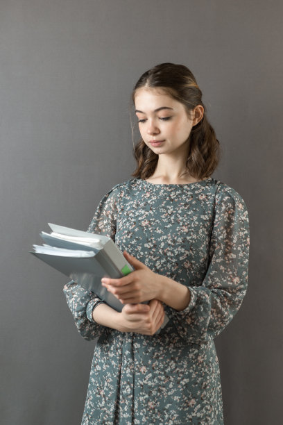 一个漂亮的成功女孩穿着裙子，站在灰色的墙上，手里拿着一叠文件夹和便条图片下载