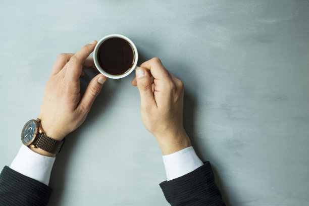 一个男人的手在灰色的背景上拿着一个热的黑咖啡杯图片下载