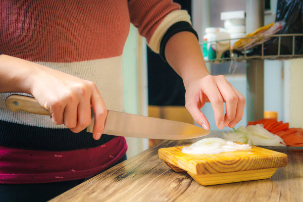 女人用刀切白洋葱，在厨房切洋葱。图片下载