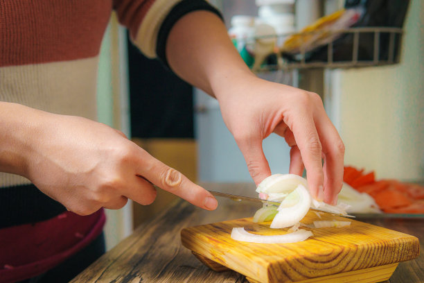 女人用刀切白洋葱，在厨房切洋葱。图片下载